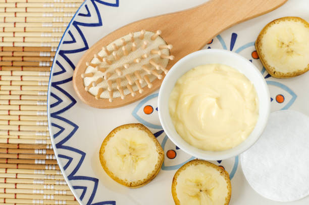 Diy banana and yogurt mask (face cream) in the small white bowl, wooden hairbrush, cotton pads and banana slices. Natural homemade hair treatment and zero waste concept. Top view, copy space máscara de plátano y yogur (crema facial) en el pequeño tazón blanco, cepillo de pelo de madera, almohadillas de algodón y rodajas de plátano. tratamiento natural del cabello casero y concepto de cero residuos. vista superior, copiar espacio