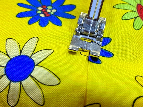 Yellow floral fabric being stitched under a sewing machine foot