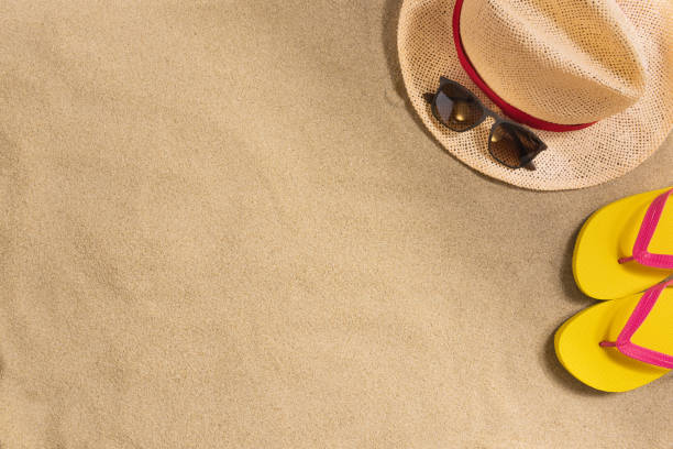 istock Summer vacation composition. Hat, sunglasses and flip flops on sand background. Harsh light with shadows. Summer background. 1217999313
