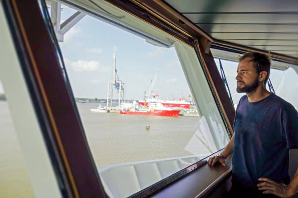 istock Man is looking from captain's bridge from large transfer vessel in port and ships getting loaded with equipment and wind-turbine parts 1218001139