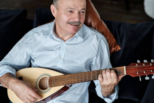 istock Elderly man on couch playing acoustic guitar staying alone at home 1218001238