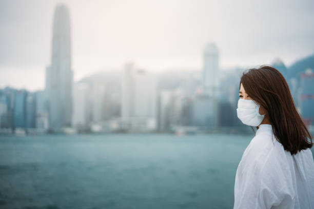 Young asian woman wearing protective face mask in city due to the polluted air or pm 2.5 and Coronavirus disease or COVID-19 outbreak situation in Hong Kong China and all of landmass in the world. Young asian woman wearing protective face mask in city due to the polluted air or pm 2.5 and Coronavirus disease or COVID-19 outbreak situation in Hong Kong China and all of landmass in the world. landmass stock pictures, royalty-free photos & images