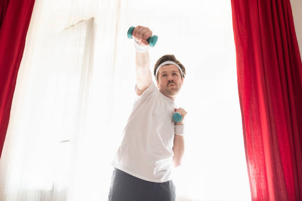 istock Funny mature man exercising at home holding weights 1218007346