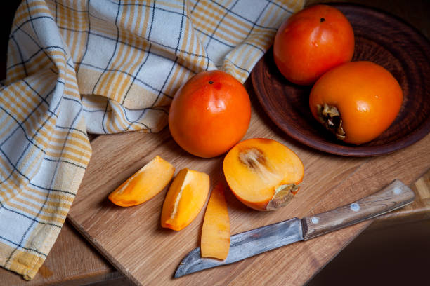 istock Whole ripe persimmon and sliced fruit on a wooden background. 1218008048