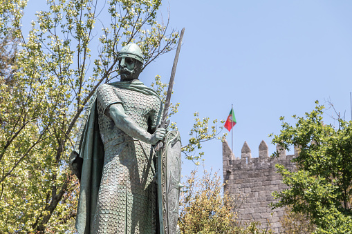 Guimaraes, Portugal - May 10, 2018: statue of the first king of Portugal, D. Afonso Henriques by the sculptor Antonio Soares dos Reis in front of the castle of Guimaraes that tourists are visiting on a spring day