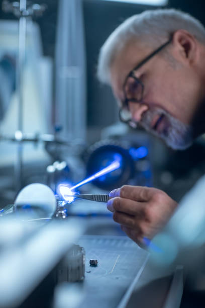 istock Portrait of Focused Middle Aged Engineer in Glasses Working with High Precision Laser Equipment, Using Lenses and Testing Optics for Accuracy Required Electronics 1218015191