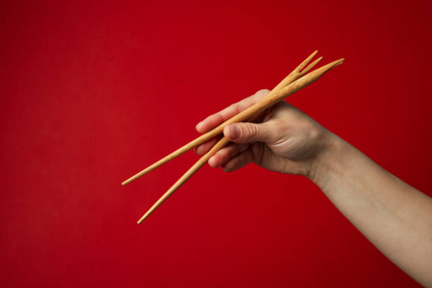 istock Female hand with chopsticks on red background, close up 1218015650