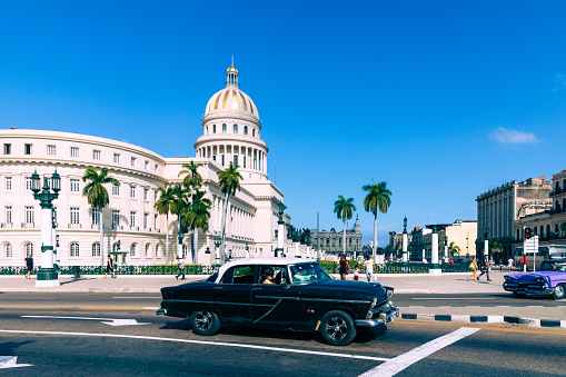 Havana, Cuba - December 10, 2019: Old classic American cars rides in front of the Capitol. Before a new law issued on October 2011, cubans could only trade cars that were on the road before 1959.