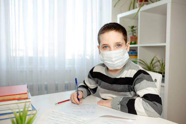 istock Sickness kid in medical mask studying and doing homework at home 1218029293
