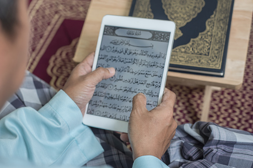 Asian Muslim man reading digital Al-Quran using tablet at home during Ramadan