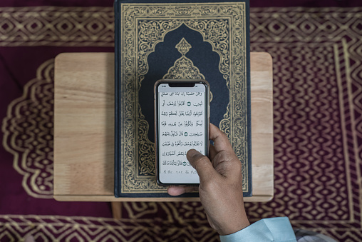 Asian Muslim man reading digital Al-Quran using smart phone at home during Ramadan