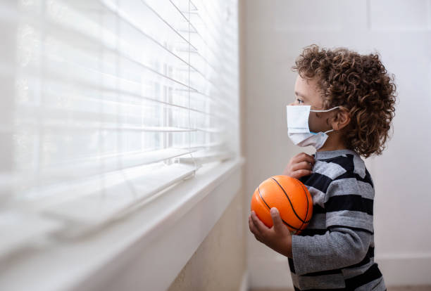 un niño mirando por la ventana con una marca protectora mientras busca protección de covid-19 - ansiedad fotos fotografías e imágenes de stock