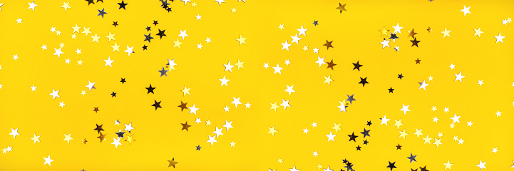 Golden and silver stars on yellow background. Flat lay, top view.