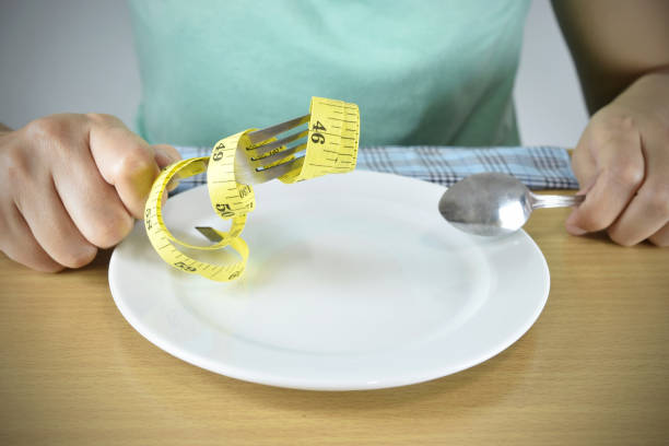 Hands with fork set and tape measure on plate.