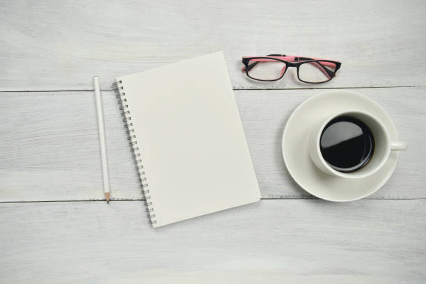 istock blank paper notebook mockup with cup of coffee, glasses on workspace. 1218037350