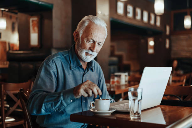 istock Elderly manager working on his laptop in a cafeteria with a cup of coffee on the table next to him 1218040749