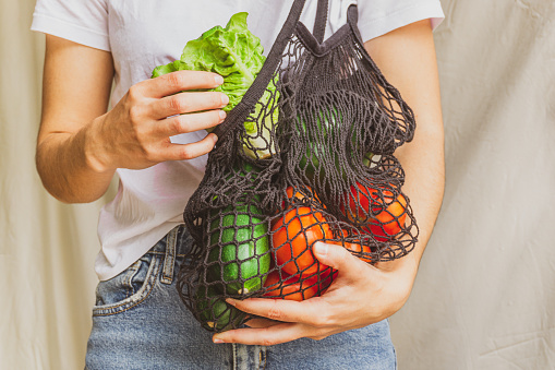 Girl holding mesh shopping bag full of vegetables and taking from inside a fresh lettuce from the farm. Sustainable, zero waste and plastic free lifestyle. Save the planet concept