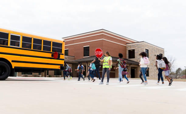 A group of schoolchildren cross a crosswalk. A crossing guard is holding a stop sign as the students cross the street.