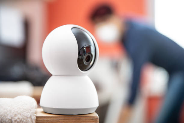 maid wearing a protective mask while cleaning living room under surveillance camera - stock photo - surveillance human eye security privacy fotografías e imágenes de stock