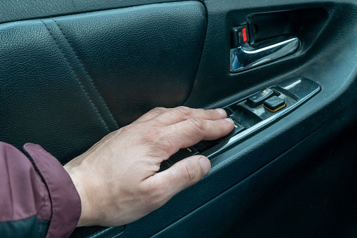 Close up male driver's hand pressing car window controls button.