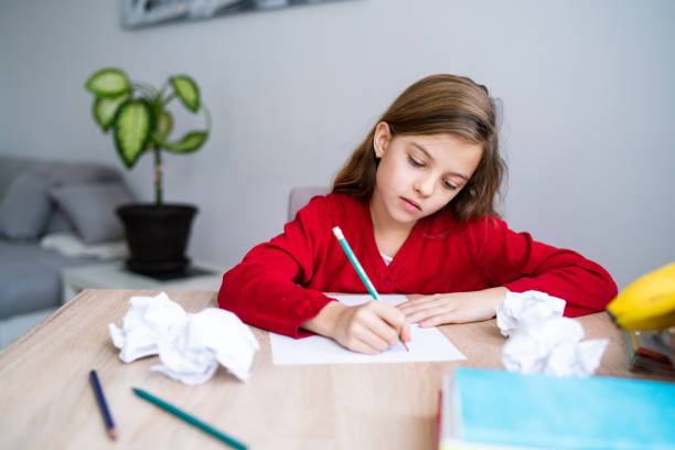 疲れた女の子はテーブルに座って宿題を書いている - crumpled paper document frustration ストックフォトと画像