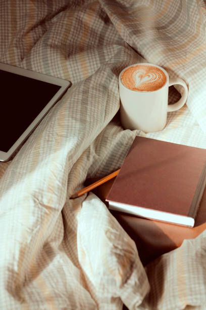 istock Notepad, book, laptop and cup of coffee on checkered textile in bed. 1218049999