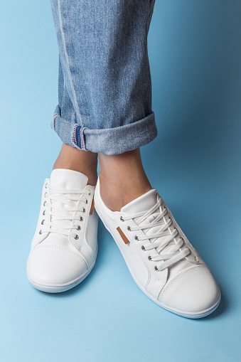 Girl's legs in jeans and white sneakers on blue background.