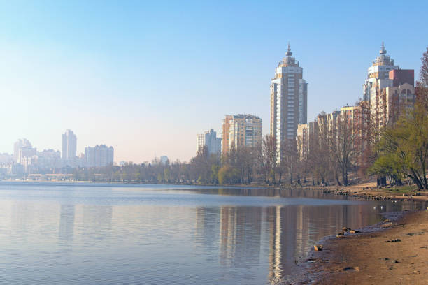 istock Scenic spring landscape view of Dnieper River and empty beach in modern Obolon district. Embankment with skyscrapers in morning smog in the background. Buildings reflected in the water. Kyiv, Ukraine 1218052260