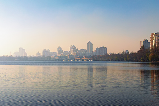Picturesque landscape view of Dnieper River and empty beach in modern Obolon district. Embankment with skyscrapers in morning smog in the background. Kyiv, Ukraine