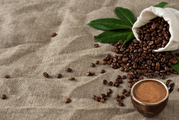 istock Cup coffee (espresso) and coffee beans in burlap sack on a burlap background. Close up, soft focus, copy space for text. Near coffee leaves. 1218053819