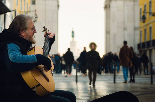 Lisbon, Portugal - February 3, 2019: dark moody portait of an old man street performer playing guitar in winter on Rua Augusta, main shopping street of Lisbon, Portugal, on february 3, 2019