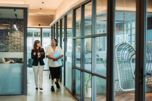 istock Two asian multi-ethnicity smiling businesswoman hand holding digital tablet and note pad having discussion, walking at office corridor 1218057361