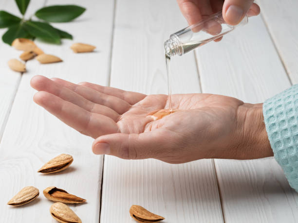 Close-up of female hands while applying moisturizing lotion or natural almond essential oil in order to repair damaged and dry skin, on white wooden background. Soft focus. stock photo
