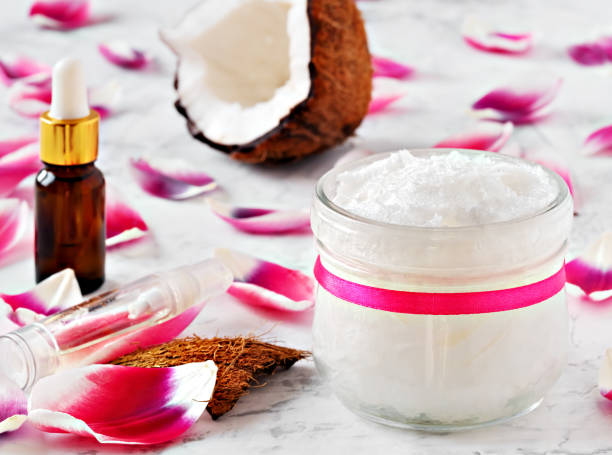 木製の白い背景上の代替療法のためのココナッツオイルとココナッツ。テーブルの上にピンクの花びらが咲きます。クローズアップ - aromatherapy oil massage oil alternative therapy massaging ストックフォトと画像