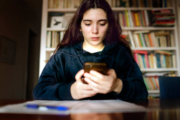 teenage girl studying with the mobile phone in the library - homework teenager mobile phone school imagens e fotografias de stock
