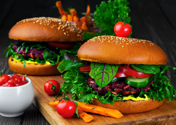 istock Freshly vegan burger with beetroot cutlets, fresh vegetable, grilled carrot, tomatoes and curry sauce. Ingredients for cooking vegetarian burgers. Herbs, spices over black wooden background. Close up. 1218071234