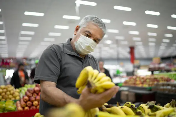 Photo of Senior man with disposable medical mask shopping in supermarket