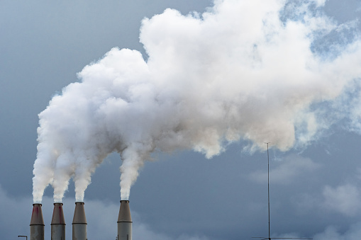 Smoke and steam rising into the air from power plant stacks; dark clouds background; concept for environmental pollution and climate change