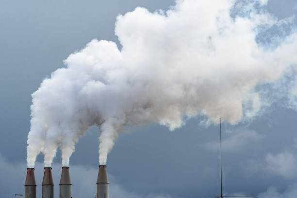 fumaça e vapor subindo no ar a partir de pilhas de usinas; nuvens escuras de fundo; conceito de poluição ambiental e mudanças climáticas - pollution coal carbon dioxide smoke stack - fotografias e filmes do acervo