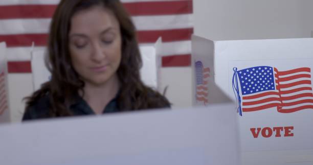 istock Focus on voting booth graphics as young woman votes in foreground 1218082504