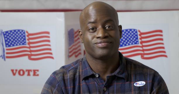 istock Black man posing and smiling in front of voting booths 1218082512