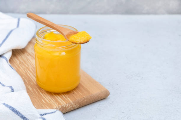 Glass jar of clarified butter (ghee) with wooden spoon on neutral concrete background. Image with copy space Glass jar of clarified butter (ghee) with wooden spoon on neutral concrete background. Image with copy space clarified butter stock pictures, royalty-free photos & images