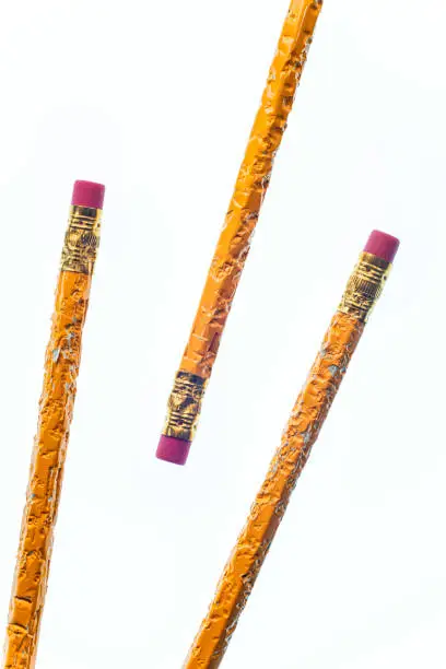 Vertical shot of the eraser end of three chewed pencils. Two are coming from the bottom left corner and the other pencil from the upper right corner.  White background.  Copy Space.