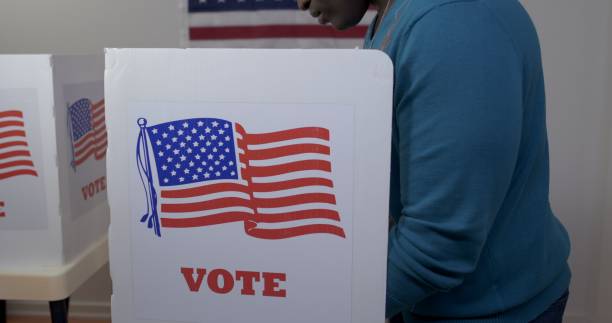 istock Side view African American man voting in booth at polling station 1218087629