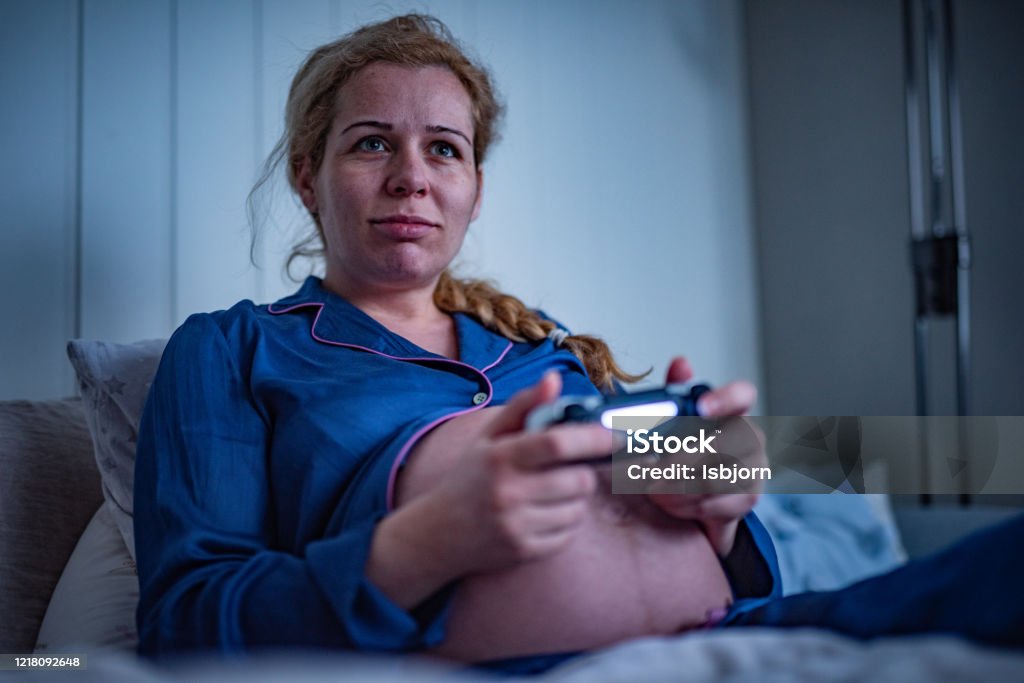 Pregnant woman playing PS4. Happy pregnant woman playing video games. Abdomen Stock Photo