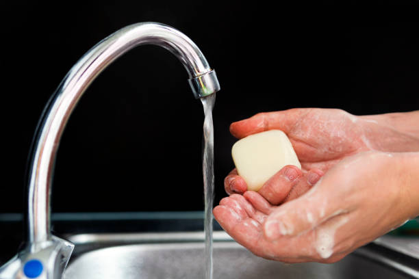 man holds in his hands soap on which water flows from metal faucet on black background. Fighting coronavirus. bar of soap in man hand in a stream of water. Prevention of viral diseases and epidemics. man holds in his hands soap on which water flows from metal faucet on black background. Prevention of viral diseases and epidemics. Fighting coronavirus. bar of soap in man hand in a stream of water. water sanitation worker washing faucet stock pictures, royalty-free photos & images