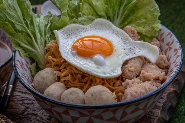 Boil egg noodles with pork ball, minced pork, fried egg, vegetables and soups in bowl and chopstick with spoon and timber background. Thai noodle soup.