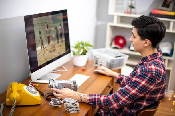 Young Woman Working From Home at her Video Editing Job Woman edits home movies in her home office during the coronavirus pandemic. She looks at the footage playing on the computer screen as she edits. female film editor stock pictures, royalty-free photos & images