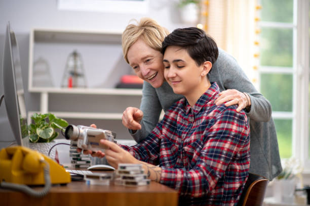 Mother Looks at her Daughter's Video Editing Job as she Works Woman edits home movies in her home office during the coronavirus pandemic. Her mom stands next to her as she shares some of the funny moments from their trips. female film editor stock pictures, royalty-free photos & images