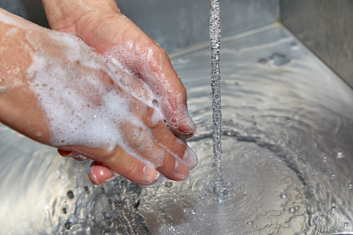 A man's hands over a sink with soap on them and water running as he is washing his hands